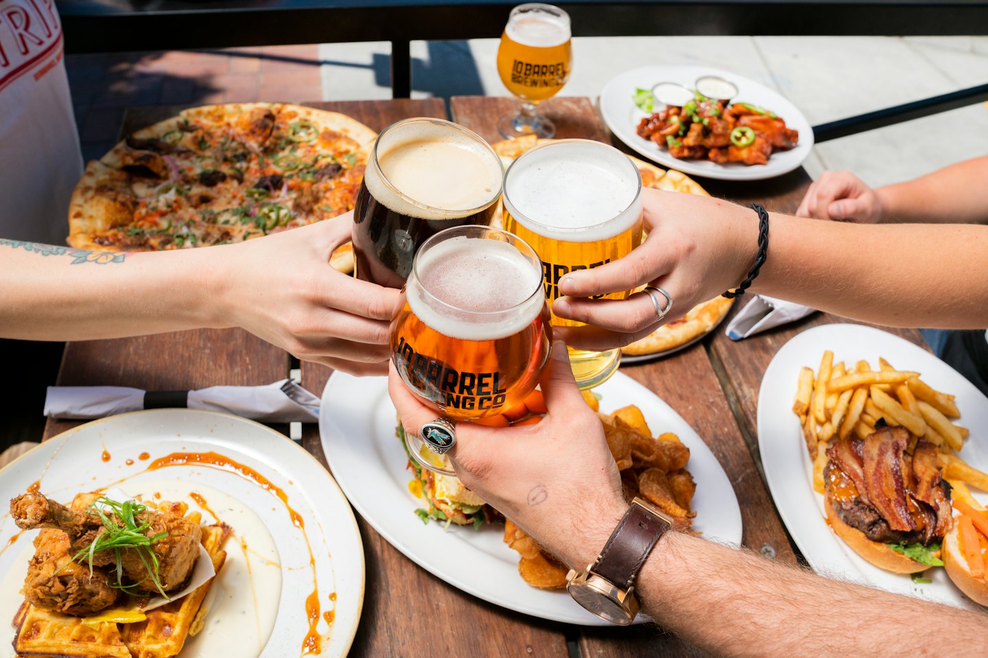 Amici che tintinnano bicchieri di birra su un tavolo pieno di cibo.