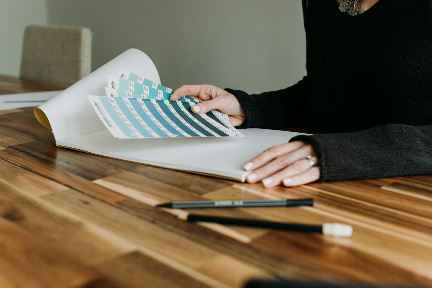 Mani creative che tengono aperto un catalogo colori Pantone su un tavolo di legno.